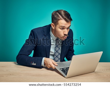 The surprised young man in a business suit working on laptop at desk on blue studio background Stock foto © 