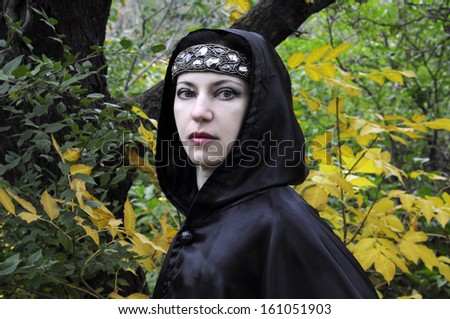 Woman with diadem under black hood in the autumn forest