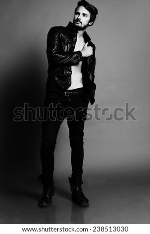 Fashion photo of sexy stylish and  handsome brunette man dressed in a black leather jacket jeans and shoes posing in studio