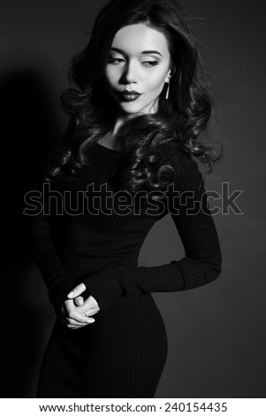 fashion photo of sexy brunette woman in black dress and heeled shoes with red lips and curly hair posing in studio