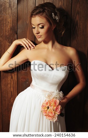 festive wedding photo of chic sexy bride in white evening dress and roses bouquet, with blond beautiful hair posing in the studio