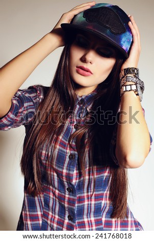 fashion swag style photo of beautiful girl with dark long straight hair in a cap,plaid shirt and watches posing at studio