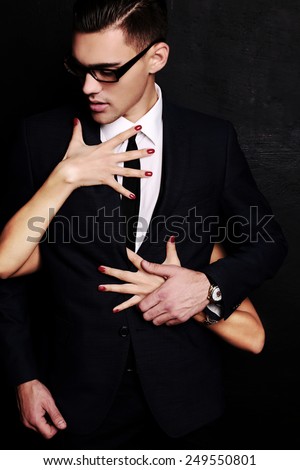 Fashion photo of office romance of sexy lovers,pretty blond woman with watch,red lipstick,and handsome brunette businessman wearing in suit,tie,glasses,they are hugging and kissing on Valentine's day