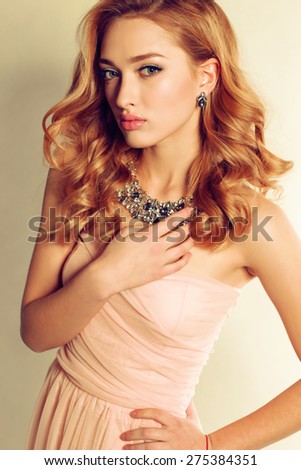Fashion portrait of sexy blond girl with curly hair wearing beautiful jewelry and posing at studio