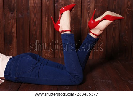 Fashion photo of woman lags wearing blue jeans and red shoes posing on the wood background at studio