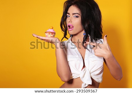 Fashion photo of  beautiful woman with brunette curls, tanned skin and slim sexy body, holding appetizing cupcake