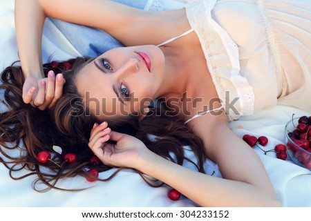 outdoor photo of a beautiful pregnant brunette woman in sarafan lying and resting on a pink blanket in the cherries