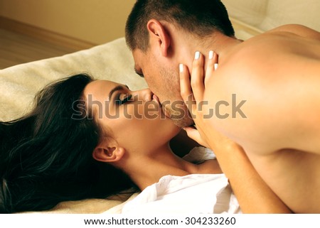 Fashion photo of sexy young brunet lovers they are hugging and kissing on a bad at home
