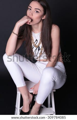 Fashion photo of sexy young brunette girl with long strait hair wearing white suit and gold chain posing at studio