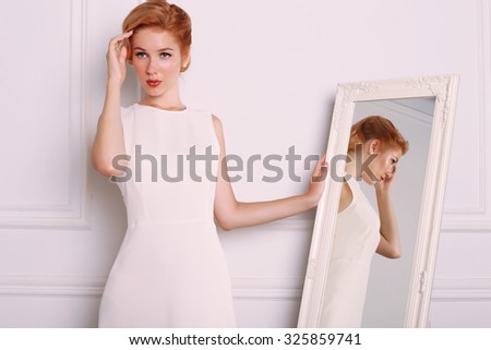 fashion photo of elegant and sexy red woman in white dress, red shoes with beautiful hairstyle posing at studio with classic interior near the mirror