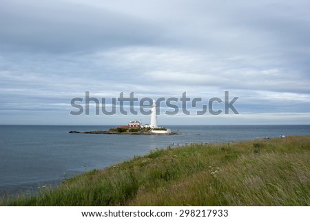 St Mary\'s Lighthouse from the grassy dunes of the cliffs.  The tide is in.