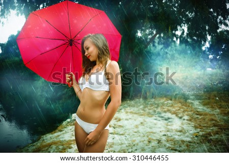 Beautiful young slim girl in lingerie standing in the rain with a red umbrella.