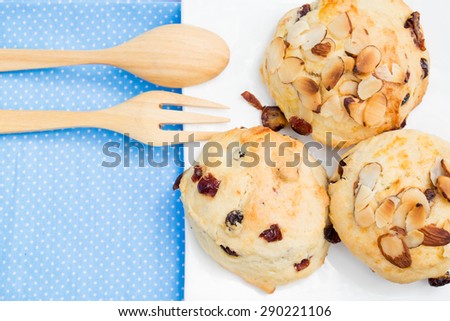 cranberry scone on the white dish, decorate with spoon and fork. However I attend to focus on cranberry more than spoon and fork