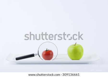 Tomato cherry re-size using magnifying glass side by side with green apple on plate with background, fruit, diet, vegetarian, and growth concept