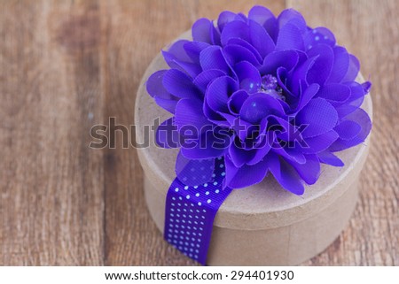 Rustic round gift box decorated with purple flower and ribbon looking from above.