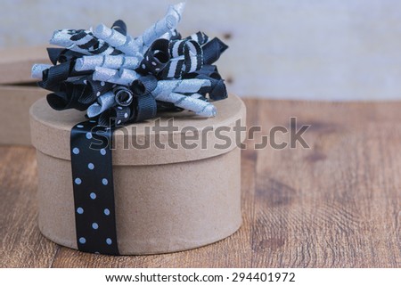 Rustic round gift box wrapped in black and white ribbon.