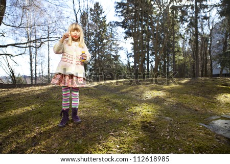 Little girl in cute clothes blowing bubbles outdoors