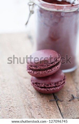 Closeup of two macaroons on wooden table with glass jar of cocoa powder in background