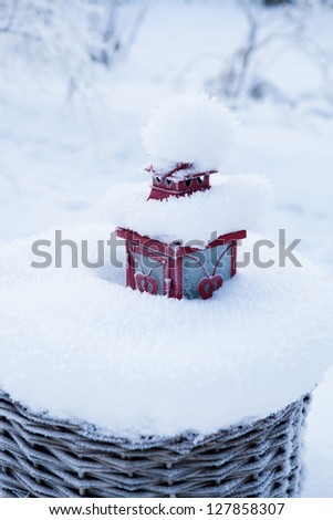 Red lantern resting in snow filled wicker basket outdoors on winter day