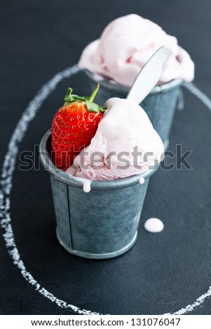 Closeup of strawberry ice cream and strawberry in two metal cups inside chalk circle on dark background