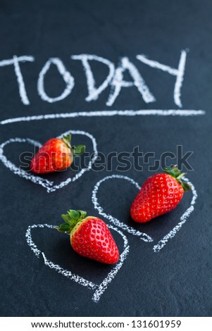 Three fresh whole strawberries inside chalk heart drawings and today word on dark background