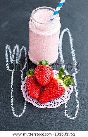 Three fresh whole strawberries and smoothie and chalk drawings of knife and fork on dark background