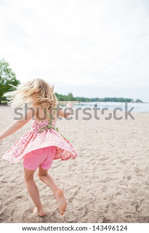 Young barefoot girl with pink patterned dress and pants having fun at beach with ocean in background