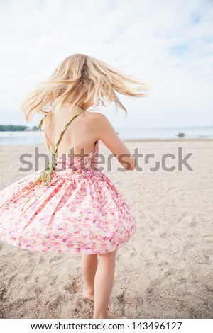 Young barefoot girl with pink patterned dress having fun at beach with ocean in background