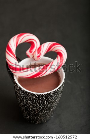 Closeup of mug of hot chocolate with hard candy heart with red swirls resting on top