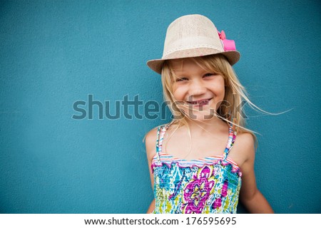 Portrait of stylish cute young girl smiling outside against blue wall background