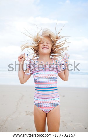 Young smiling cute girl in swimming suit having fun at the beach with eyes closed and hair moving