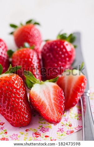 Closeup of bunch of fresh strawberries and silver metal knife resting on decorative floral serviette