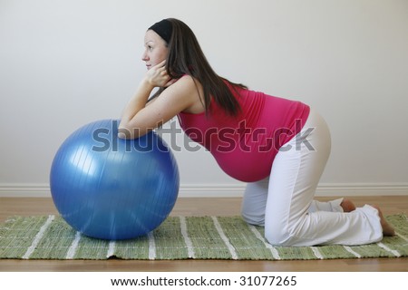 A young pregnant woman in a pink shirt doing an abdominal muscle exercise using a blue fitness ball.