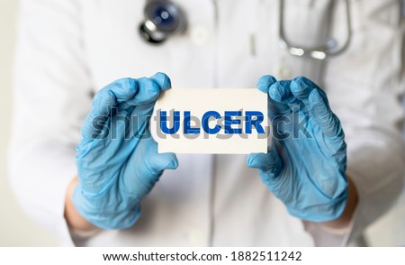 A medical worker in gloves holds a card with the words ULCER. Medical concept.