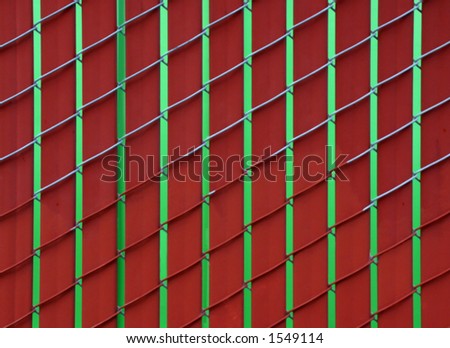 Red slats in a chain-link fence. Green dumpster behind the fence.