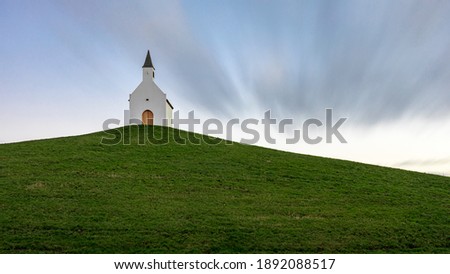 A Small white church on top of a grassy hill. It's a long exposure shot on a partly clouded day. Stock fotó © 