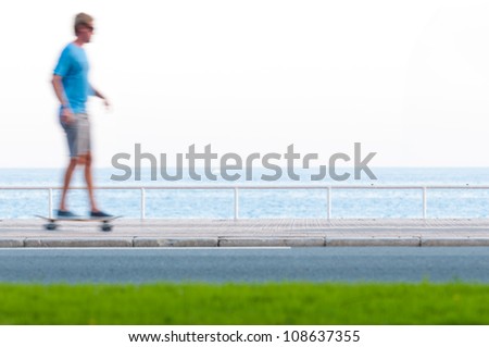 Man on skate board at the seaside. Motion blur. Car road in foreground and sea and sky in background. Cote d\'azur, Nice, France.