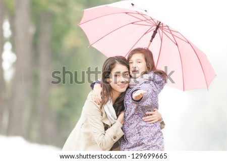 Young beautiful woman with pretty little daughter in park under umbrella. Mother and daughter together. Friendly family being happy and cheerful. Family outdoor in rain.