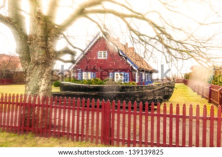 Lovely dark red country house with shutter windows and big yard paled with wooden fence. Large bare tree with long branches and fence in foreground. Quiet rural place. Traditional russian house.