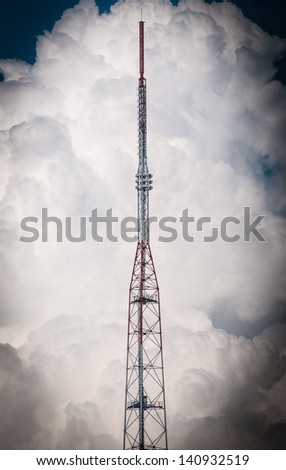 High red and white television tower. Blue sky with clouds in background. Modern wireless technology for telecommunication. Silhouette of tall modern construction. Station for global broadcasting.