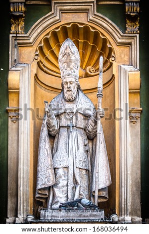 Detail of Nice Cathedral facade in close up view - catholic priest statue with staff in hand under yellow arch. Priest sculpture as part of church exterior. Architecture of Europe, France.