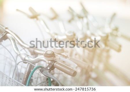 Vintage bicycles standing in row one after another. First bike with classic straight handle bar, hand-brake and bell in foreground, other vehicles blurred. Retro style objects. Sport and activity.