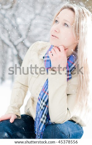 young girl in snow in winter street sitting on the bench