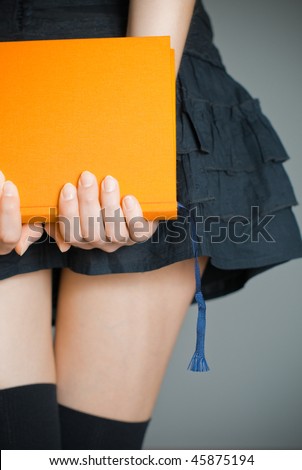 view of the lower body part of woman wearing skirt and stockings holding book in her hands