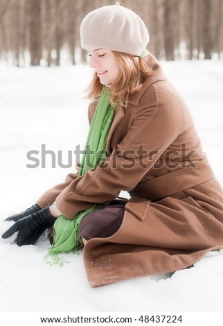 winter portrait of young and beautiful natural looking woman in casual clothes sitting in snow and making snowball