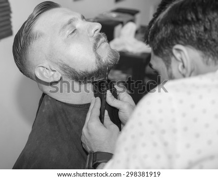 Grooming the beard. Barbershop. Man hairdresser doing haircut beard adult men in the men\'s hair salon. Hairdressers in the workplace. Barber. Grooming the beard. Barbershop. black and white