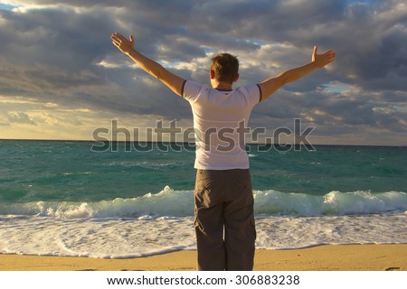 Man raising hands and open arms. Happy lifestyle man when sun rising up or sunset. Man, sea, sun, sky, clouds, mountains, ocean - the concept of the free way of life. Downshifting. Travel, vacation.