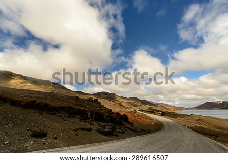 road and a lake under blue sky with clouds