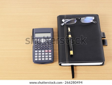 Calculator and Business book with Fountain pen and eyeglasses on wooden desk
