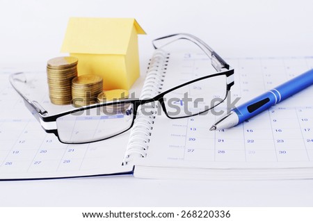 Loan concept with Eyeglasses and pen and coins stack and paper house on book pages